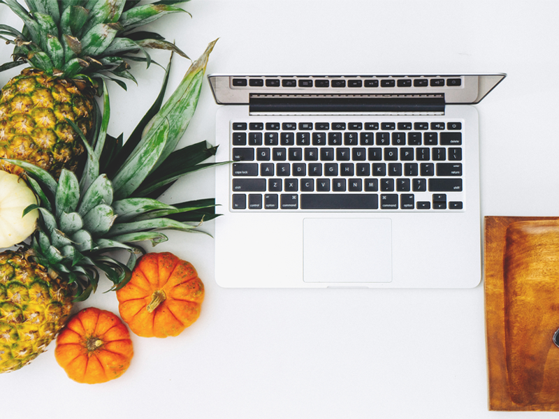 Laptop auf einem Tisch, daneben Ananas und kleine Kürbisse